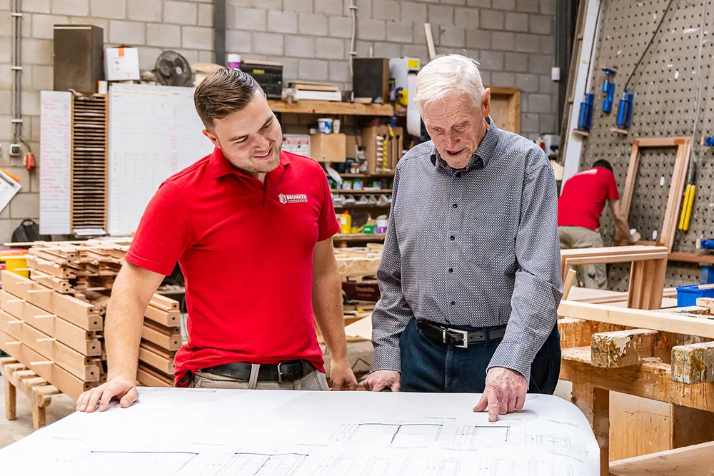 Timmerman en senior vakman bespreken een bouwtekening in de werkplaats