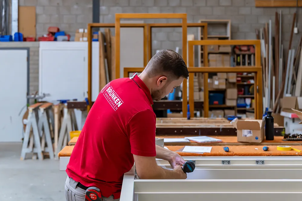 Timmerman van Brünken monteert een nieuw wit houten kozijn bij het vervangen van kozijnen