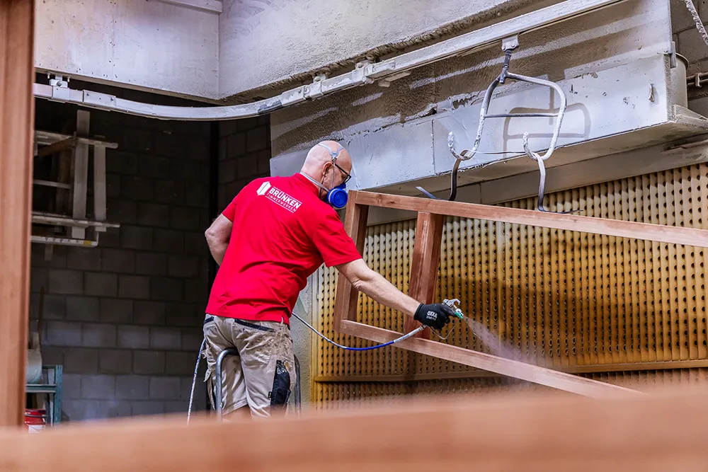 Timmerman spuit een houten kozijn in de spuitcabine